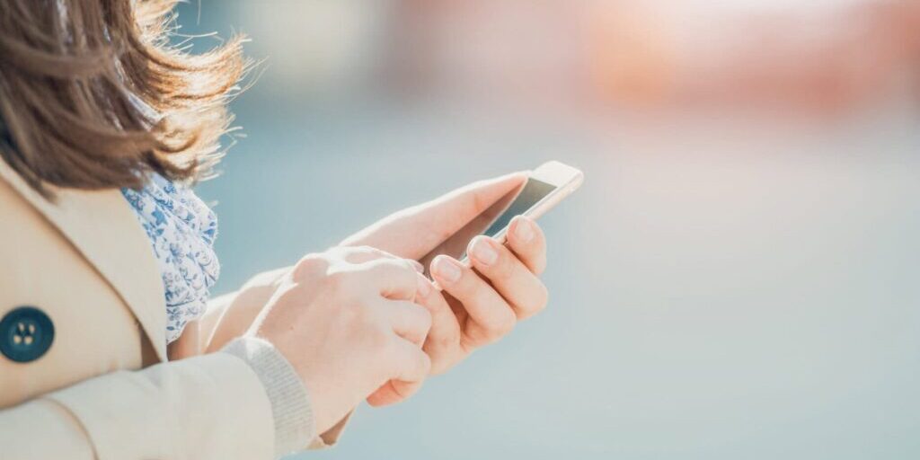 Young woman walking and using a smart phone on a city street.